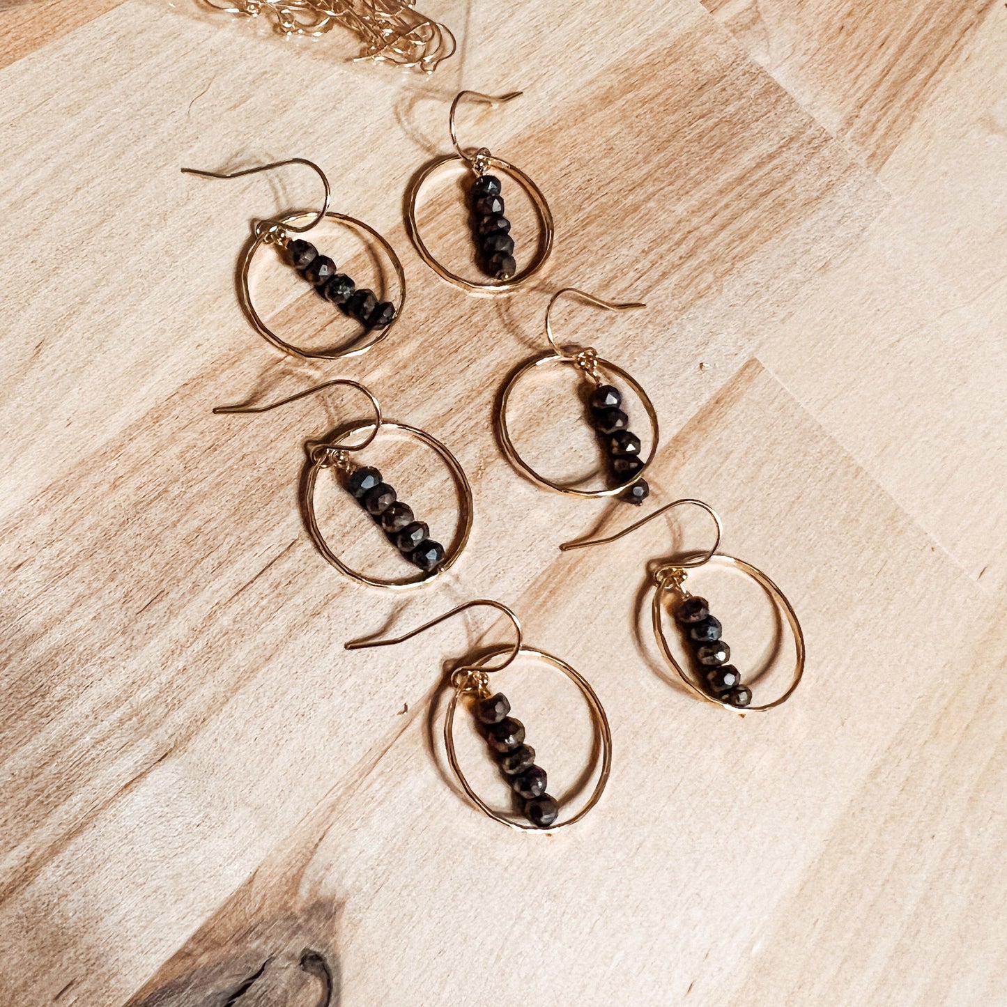 Gold circle earring with black bead pyrite stones on wood table top 