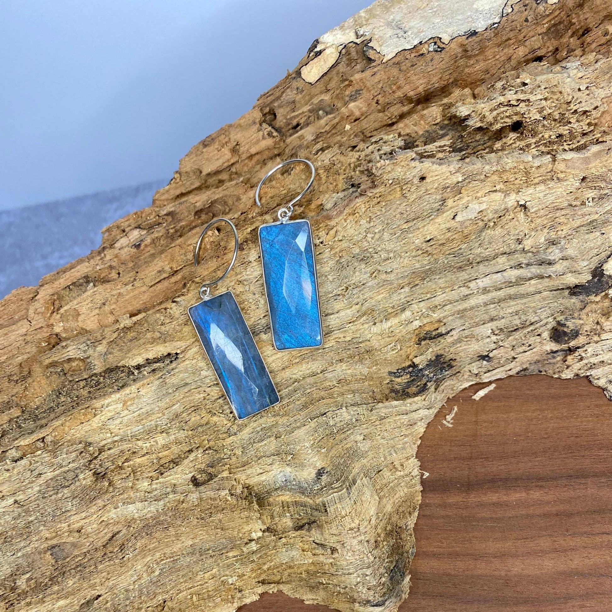 rectangle labrodorite earrings with sterling silver on a piece of drift wood on top of a wood table with blue background