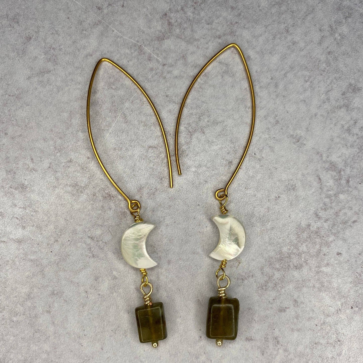 two gold earrings with mother of pearl gem and labrodorite gems hanging on gold metal with white stone background