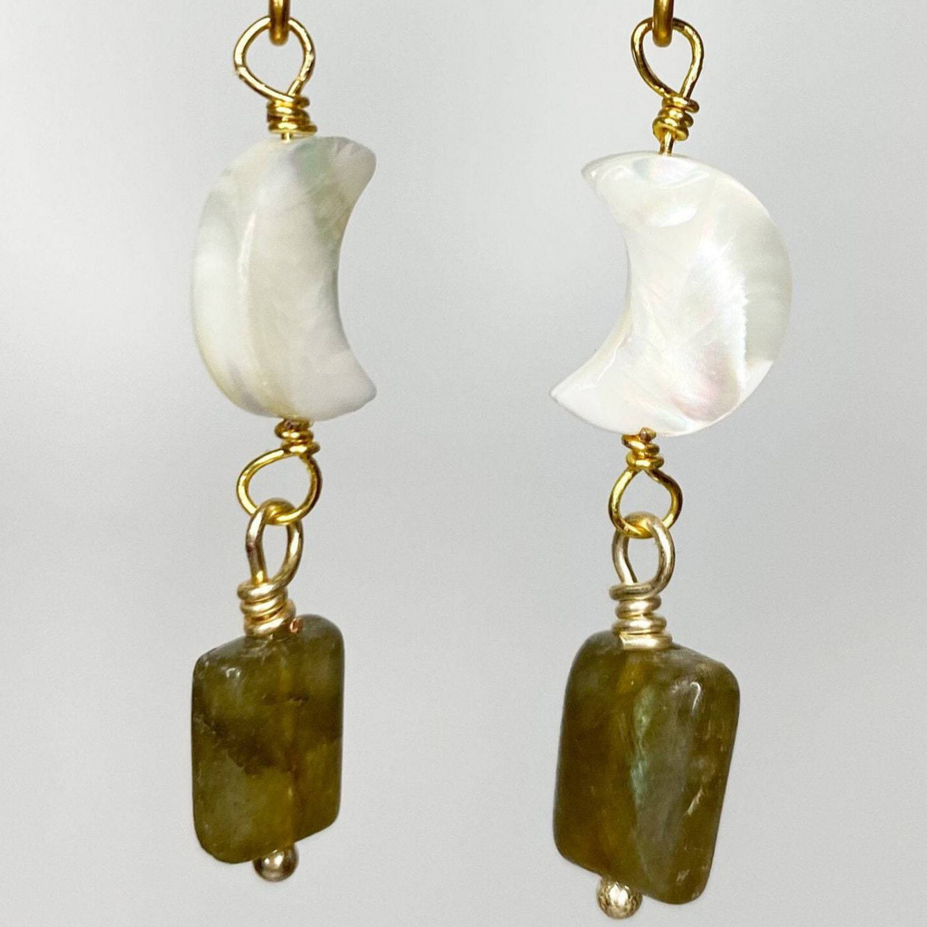 two gold earrings with mother of pearl gem and labrodorite gems hanging on gold metal with white background