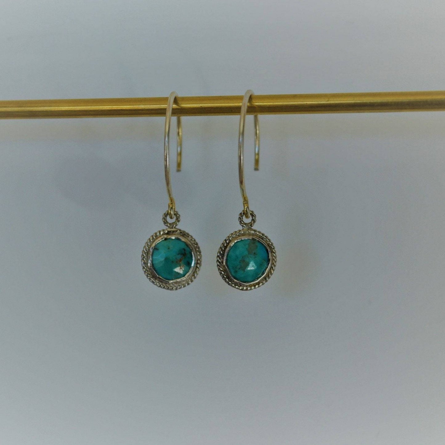 Arizona Turquoise Gem surrounded by sterling silver hanging on sterling silver metal hanging on gold bar in front of white background