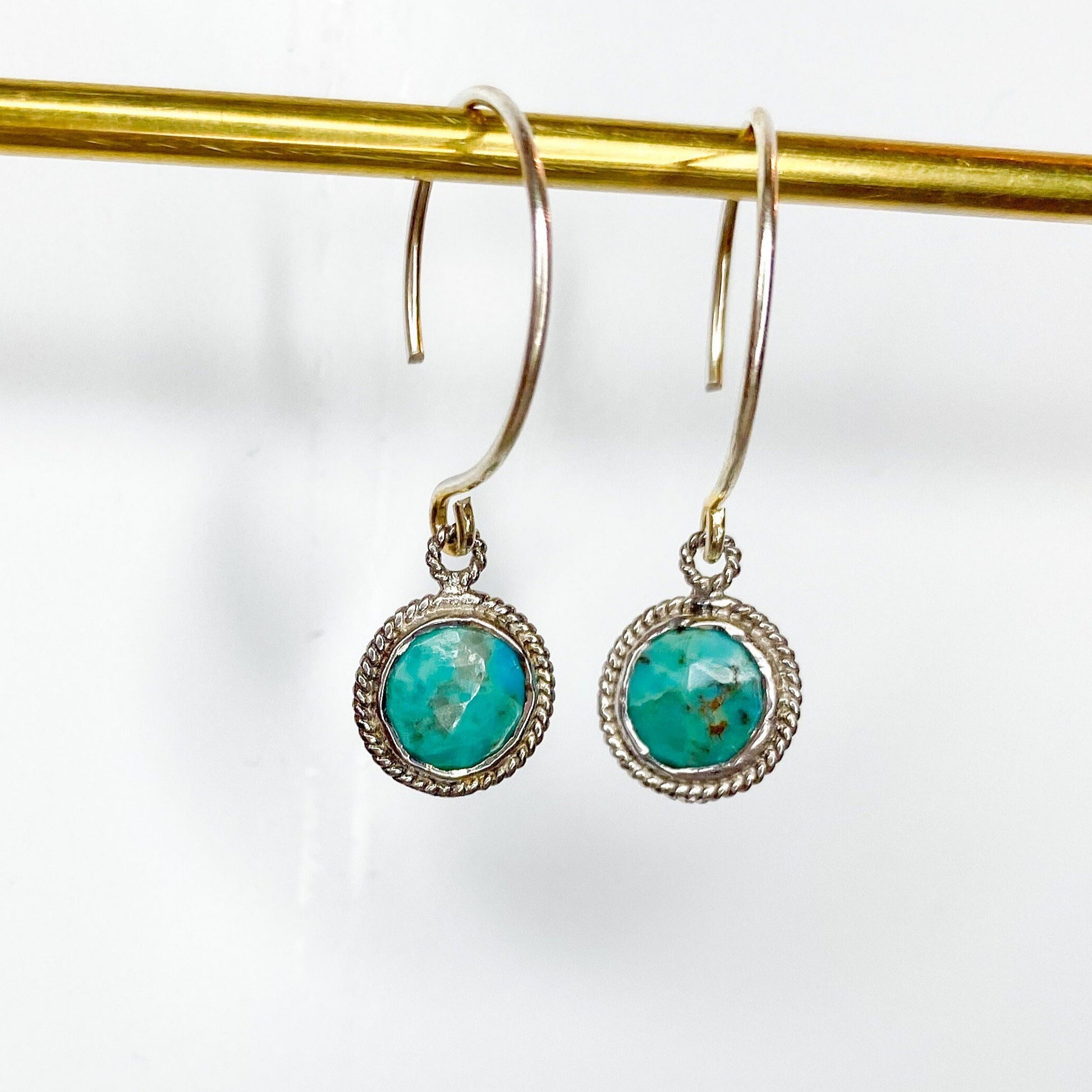 Arizona Turquoise Gem surrounded by sterling silver hanging on sterling silver metal and a gold bar in front of a white background