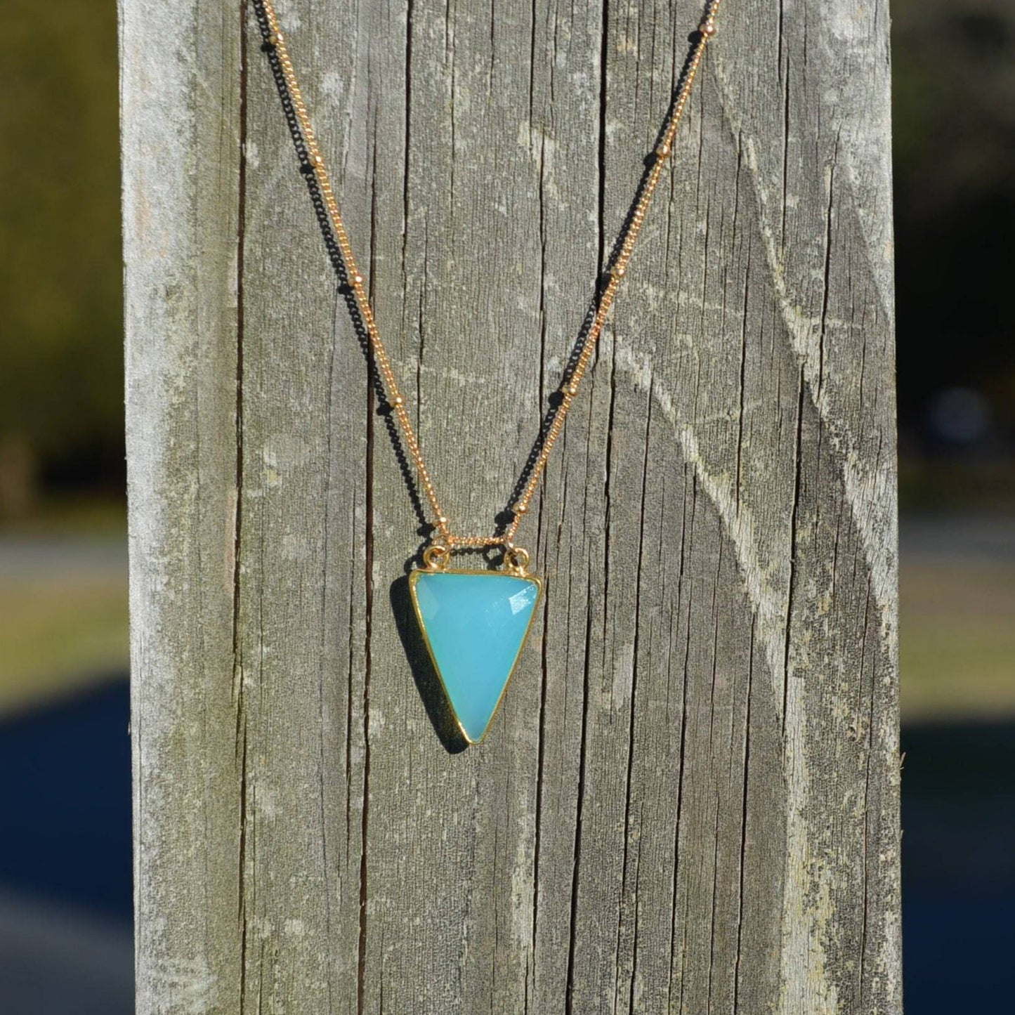 aqua chalcedony arrowhead pendant hanging on hold beaded necklace on reclaimed wood fence with blurred background