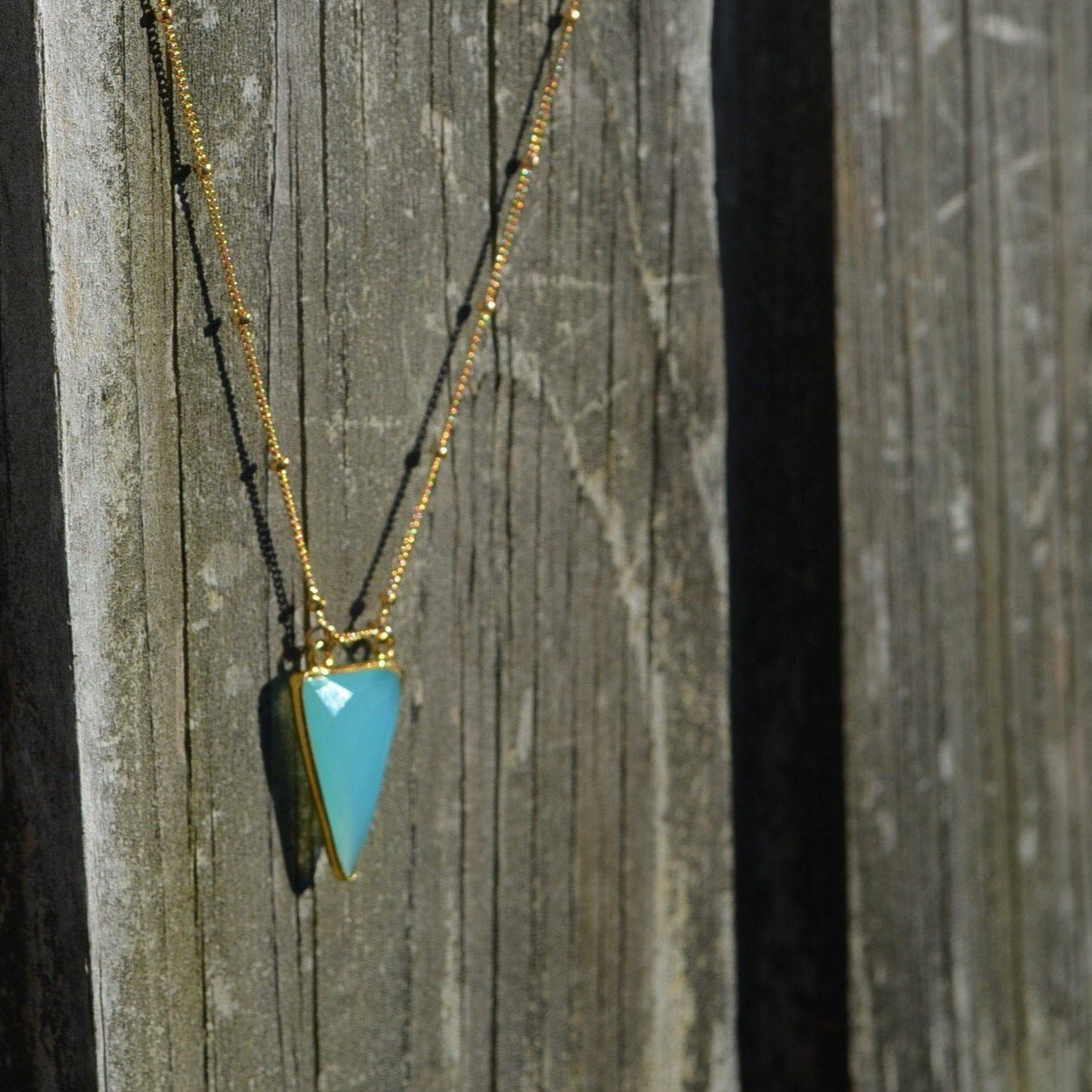 aqua chalcedony arrowhead pendant hanging on hold beaded necklace on reclaimed wood fence