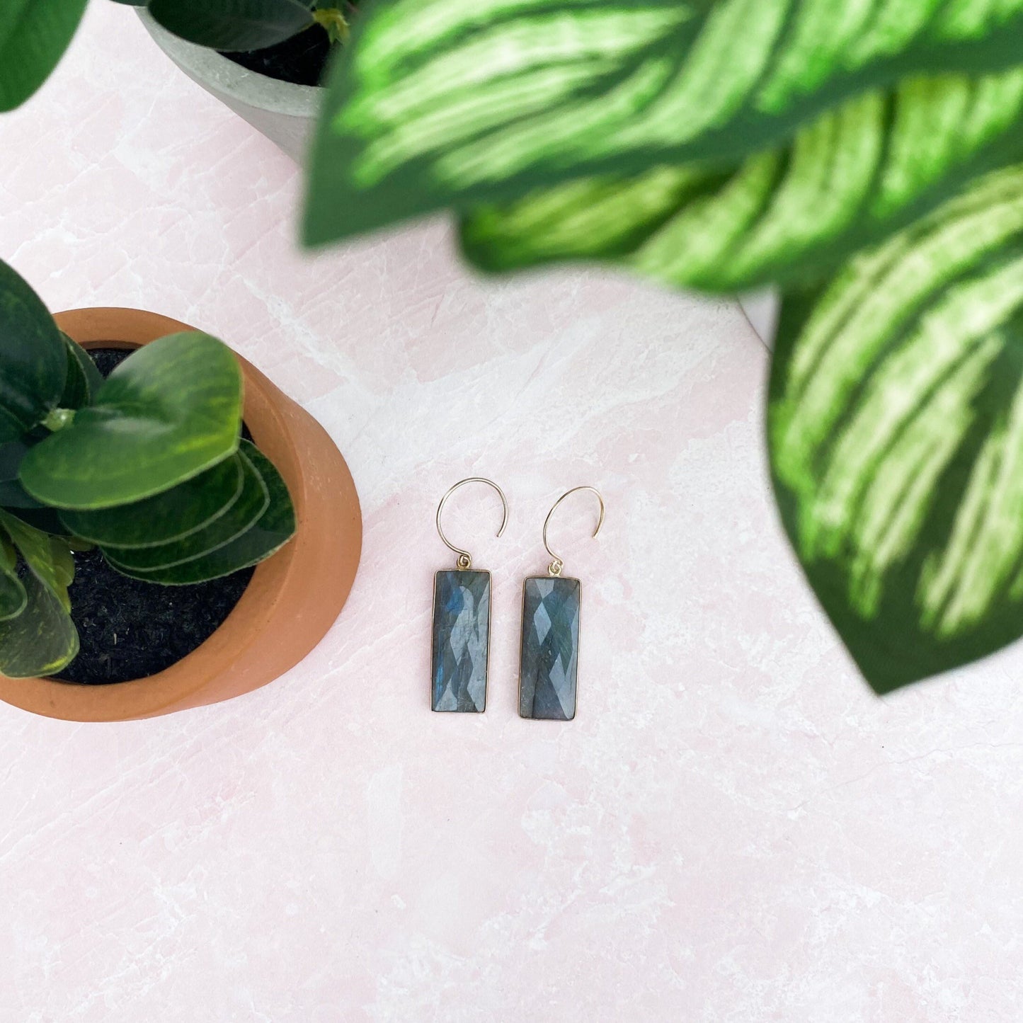 rectangle labrodorite earrings with gold metal on a white quartz table surrounded by green plans in tan pots