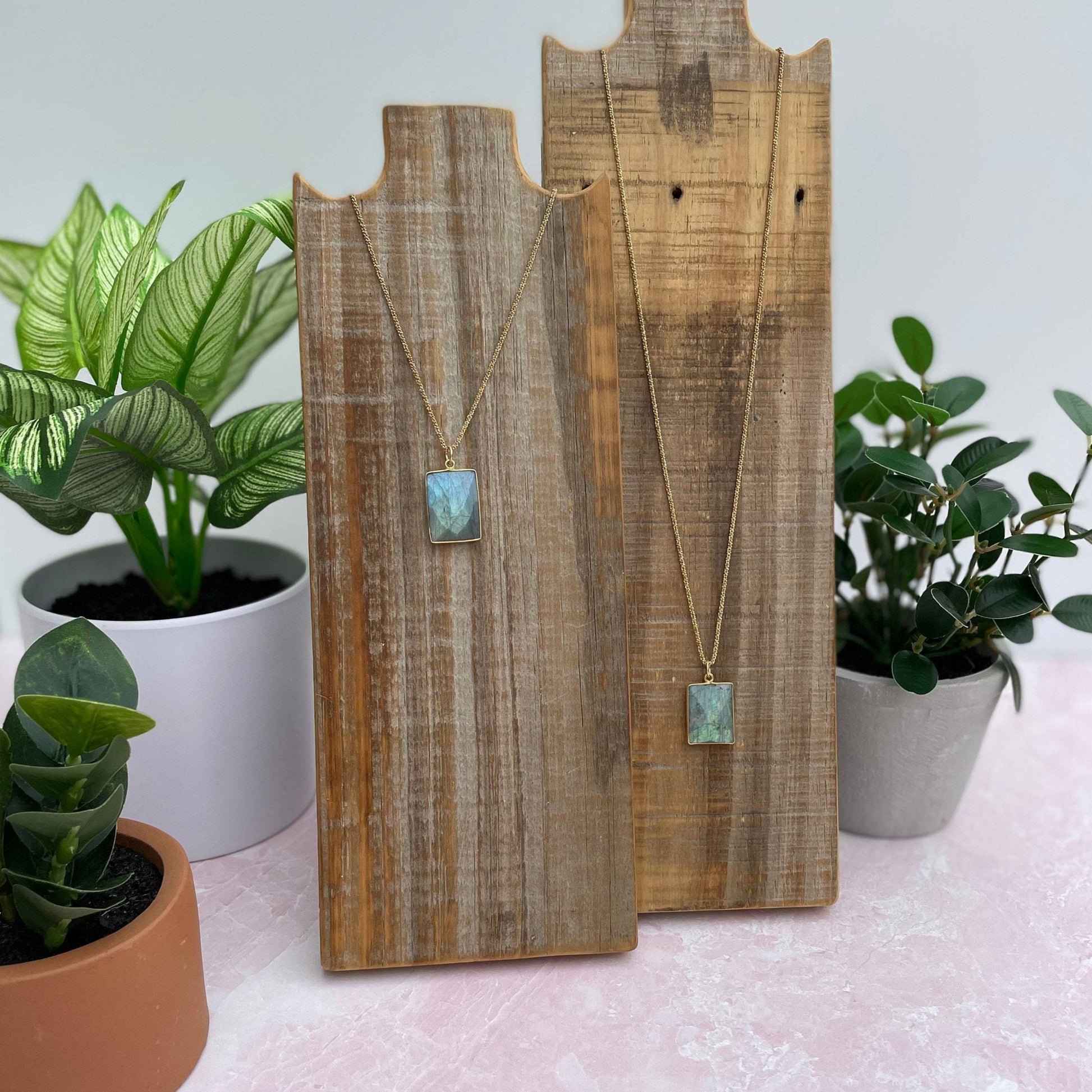 beautiful blue square labrodorite bezzel pendent hanging on gold chain hanging on reclaimed wood next to another gem hanging on gold chain on reclaimed wood