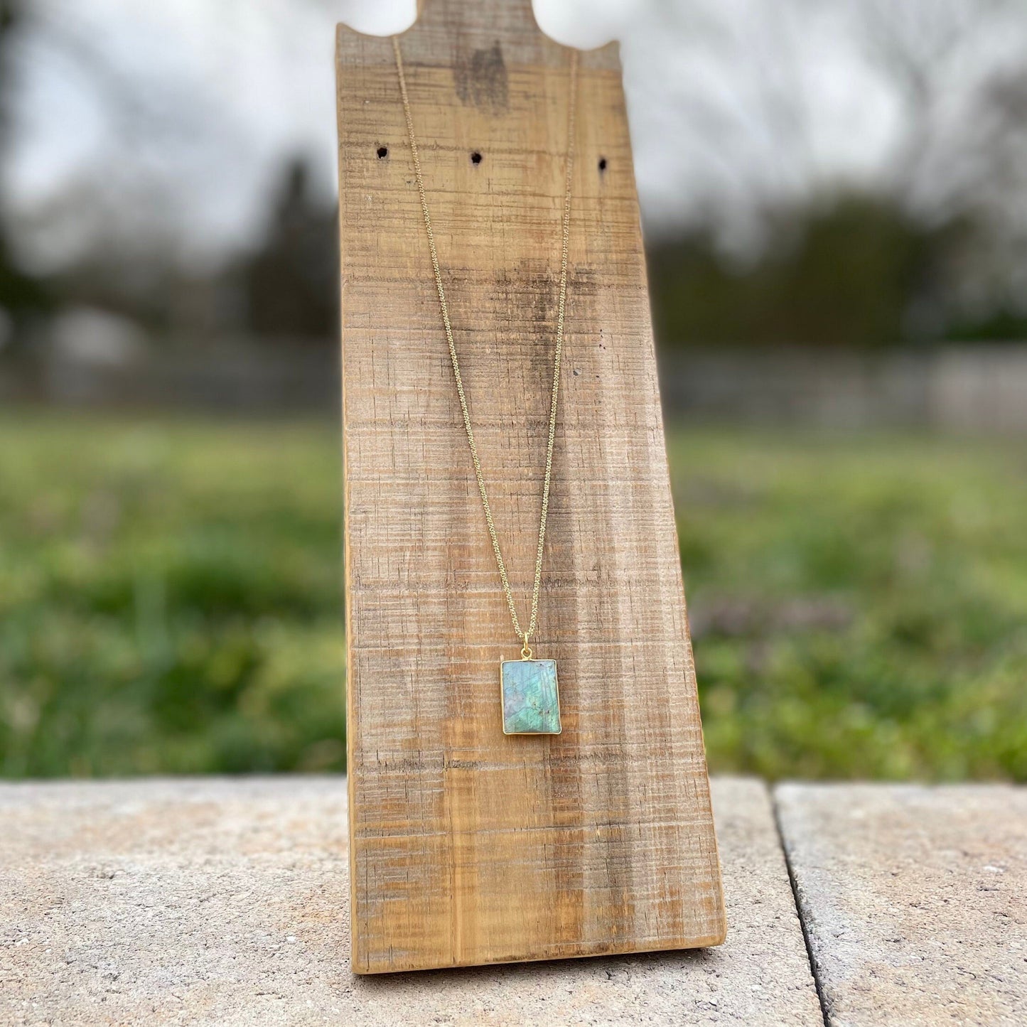 beautiful blue square labrodorite bezzel pendent hanging on gold chain hanging on reclaimed wood 