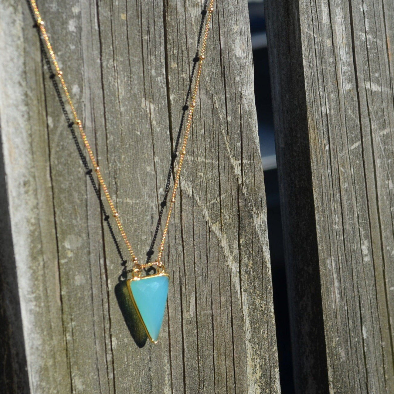 aqua chalcedony arrowhead pendant hanging on hold beaded necklace on reclaimed wood fence